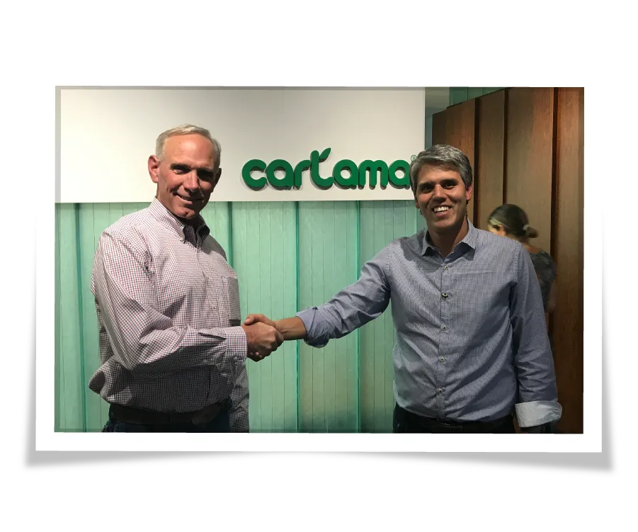 Two men shaking hands in front of a "Cartama" logo sign