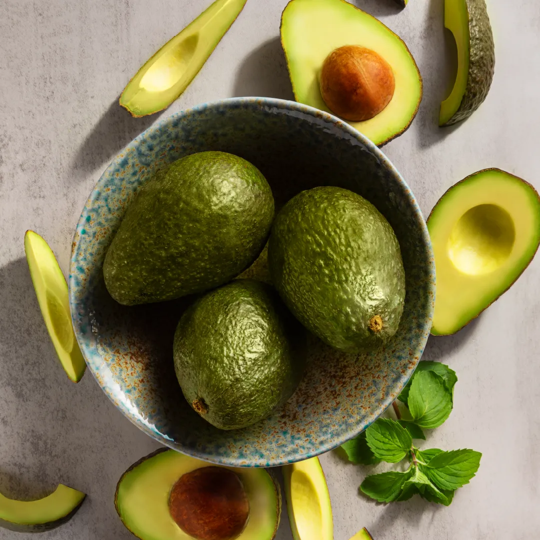 full avocados in a bowl surrounded by cut avocados