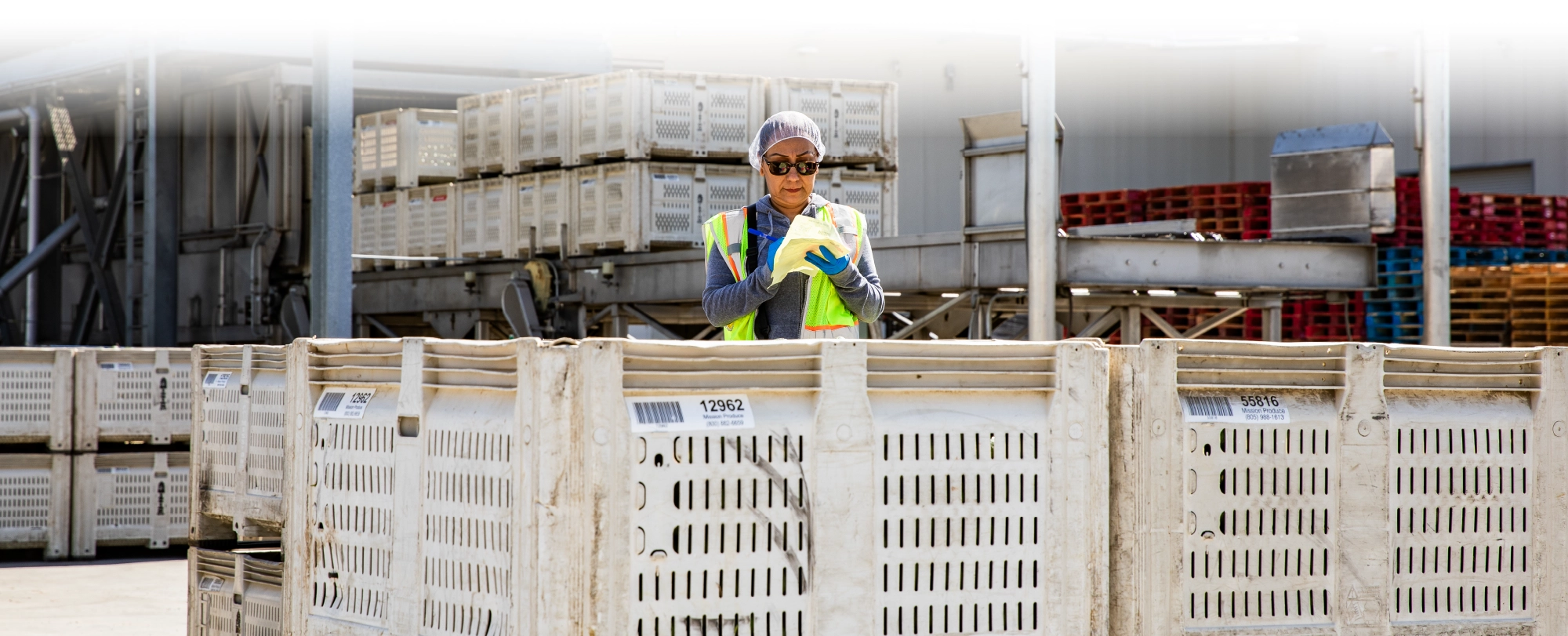 Mission Employee writing on a form surrounded by crates in warehouse